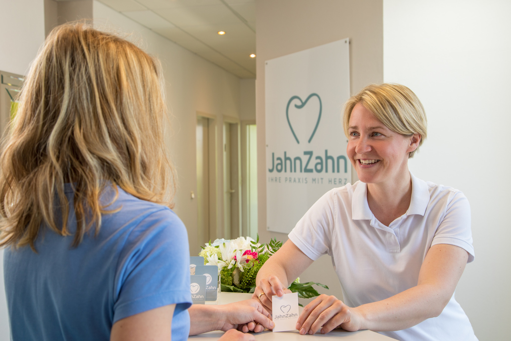Carolyn Jahn überreicht Patientin eine Visitenkarte am Empfang